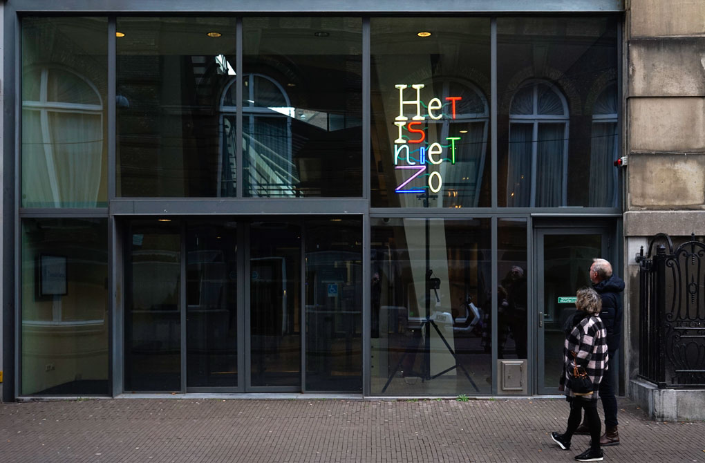 In gekleurde neonletters op een vier meter hoog statief staat Het is niet zo. Het kunstwerk staat bij ingang van het Logement van de Heeren van Amsterdam. Het is het gebouw waar de Parlementaire Enqute Commissie van de Tweede Kamer zitting heeft. Het kunstwerk is gefotografeerd na de restauratie op 13 december 2022