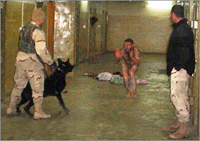 Man bedreigt liggende naakte man met aangelijnde herdershond. Locatie is gang Abu Ghraib